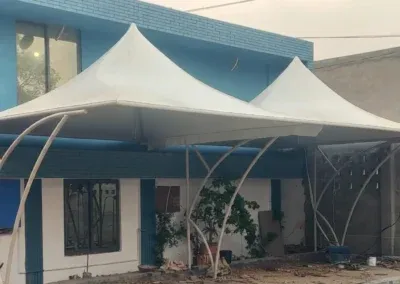 Twin-peaked fabric canopy on branching supports beside a blue building